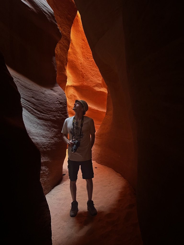 Anthony with a camera, looking up through an orange slot canyon