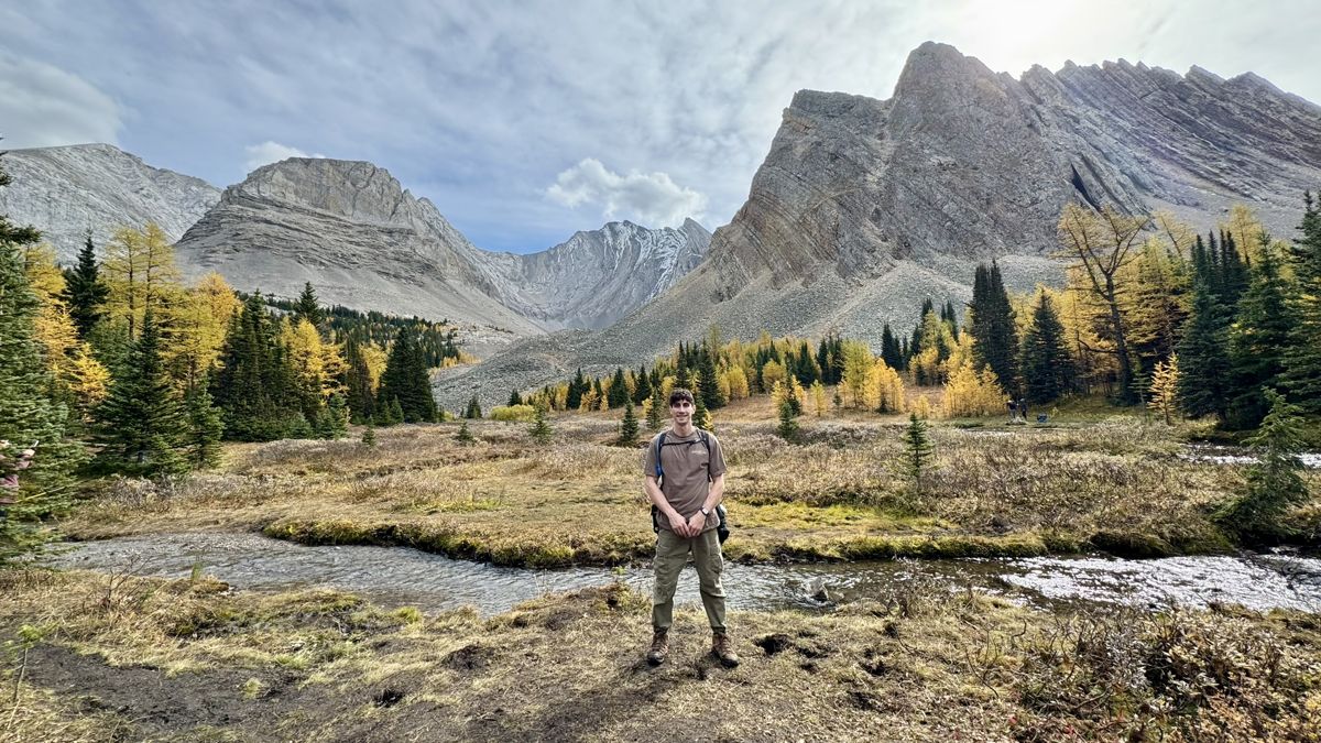 Anthony on a trail below rocky peaks and golden larches