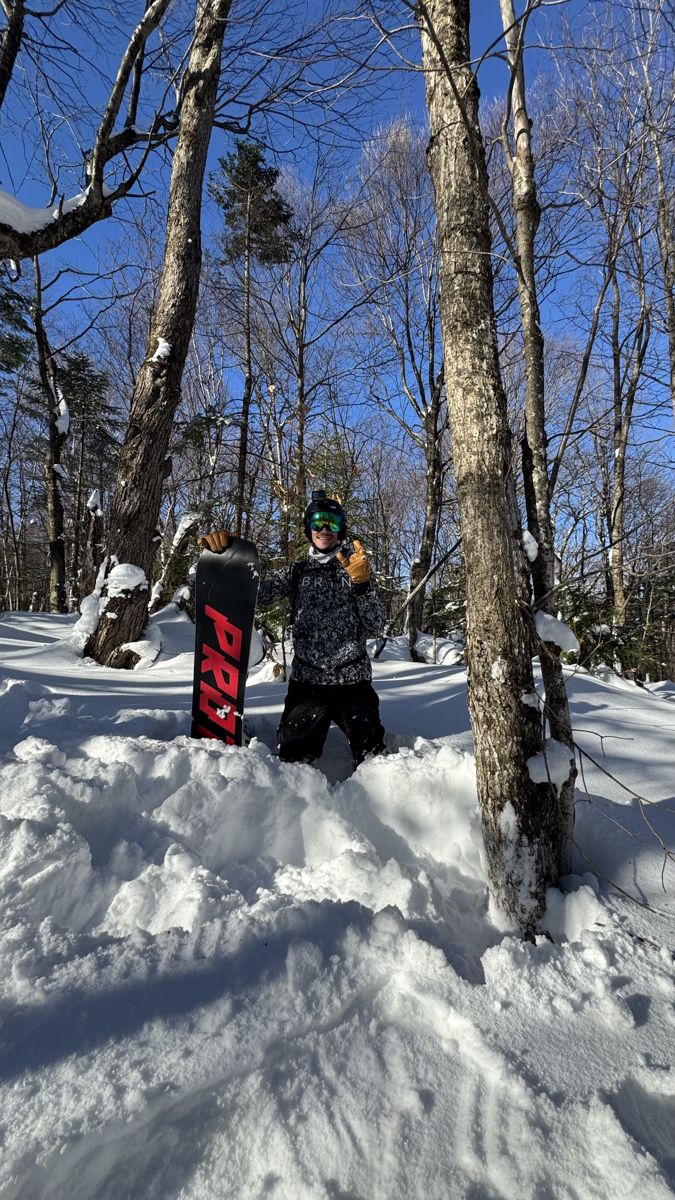 Anthony standing in deep snow among the trees, holding his snowboard